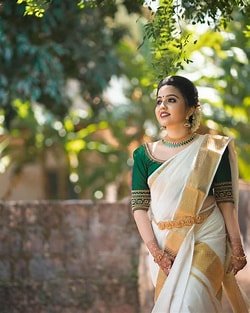 Traditional Kerala Style Sarees with Elegant White Kasavu Design Woman wearing traditional Kerala style sarees with a classic white Kasavu saree and green blouse outdoors